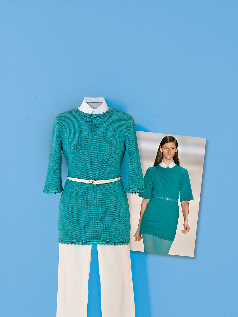 Turquoise knit sweater with white pants and belt on blue background