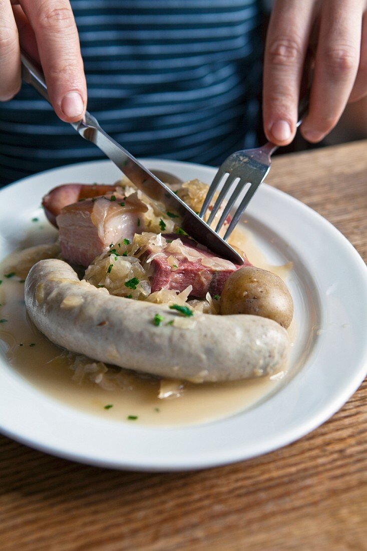 A man eating sauerkraut with white sausage and salted leg of pork