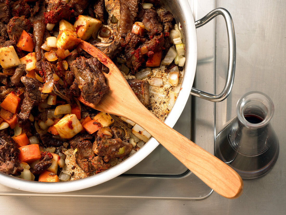 Close-up of meat in juniper sauce in casserole with wooden spoon, step 1