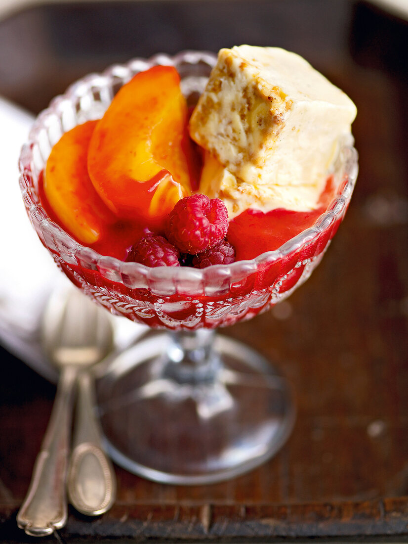 Glass of peach melba with raspberry sauce and krokant parfait on wood