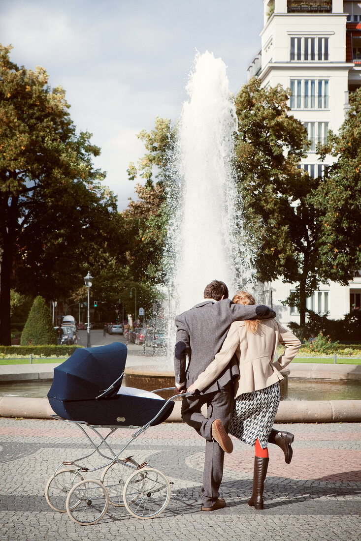 Rear view of couple facing fountain and standing with pram