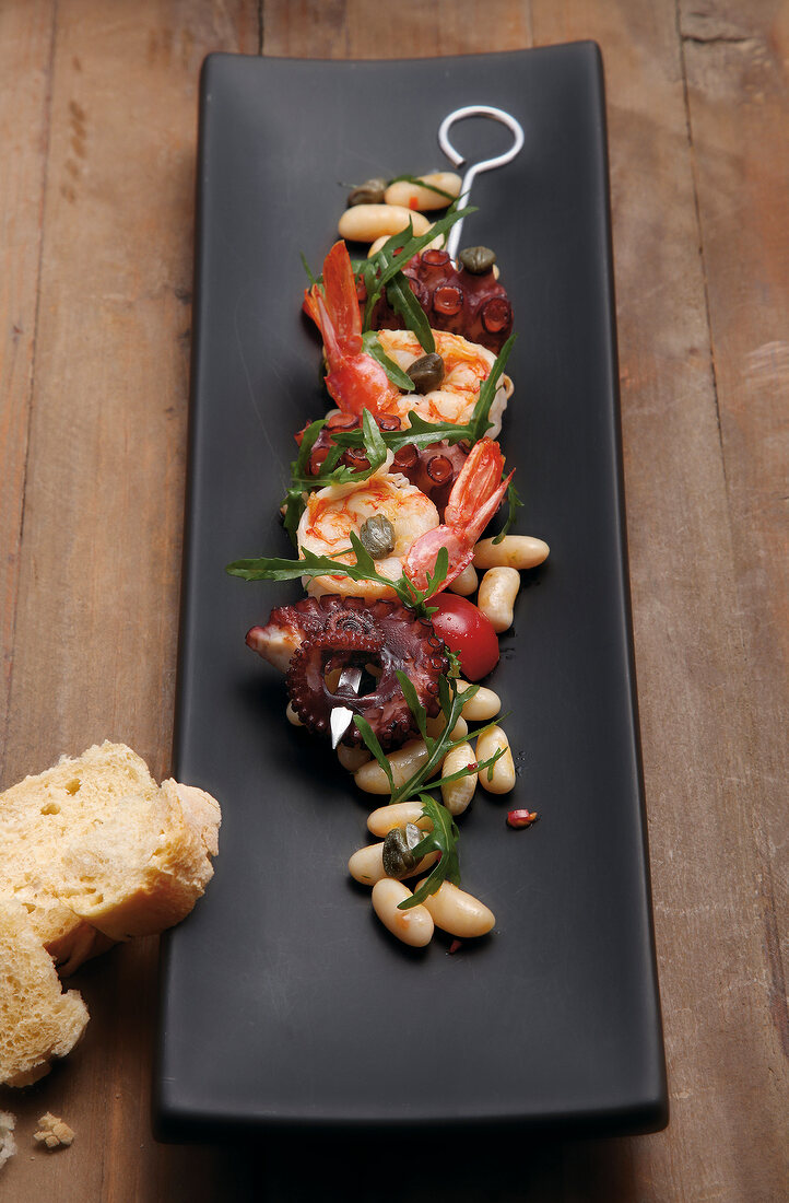 Shrimp and octopus skewers with salad of white beans in serving dish