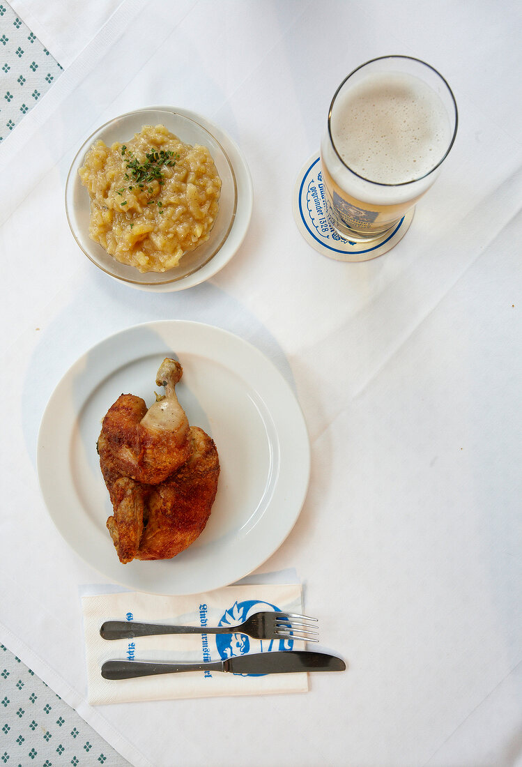 Munich, half chicken, potato salad and beer on white surface, overhead view