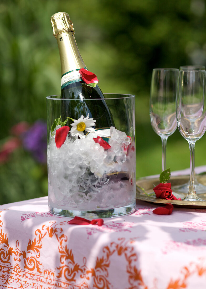 Close-up of champagne bottle with ice in jar and two wine glasses on table
