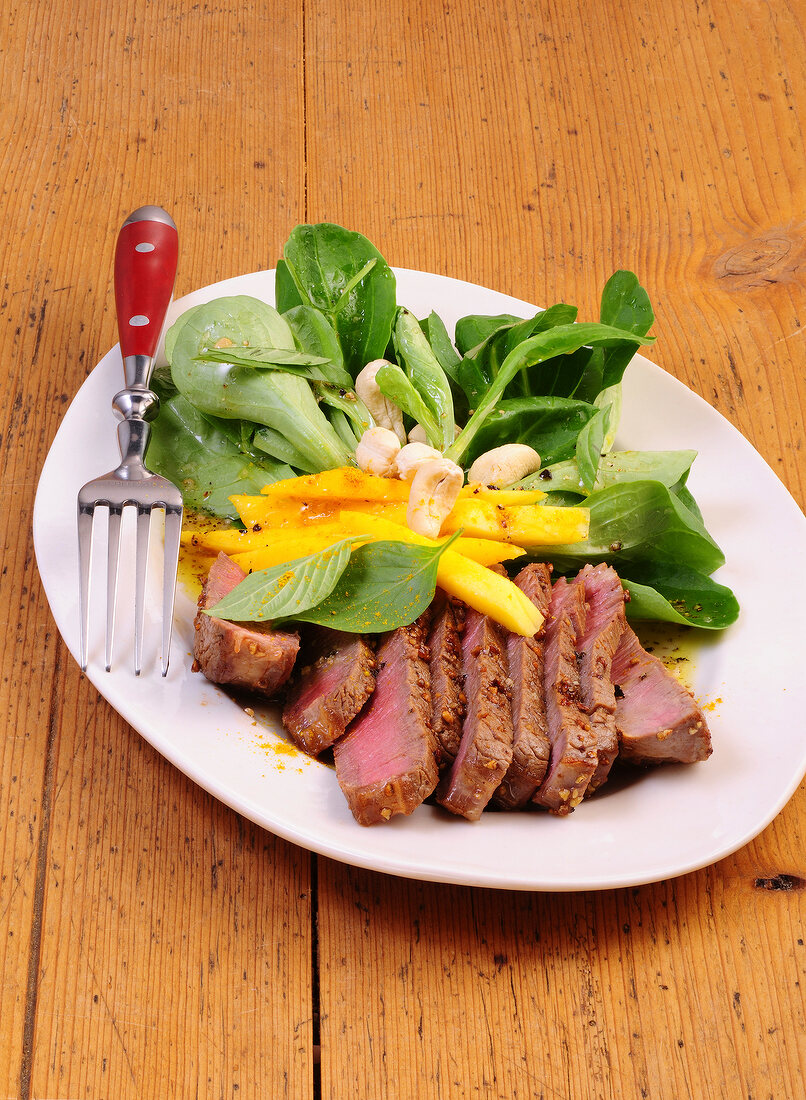 Lamb's lettuce with slices of mango and steak in serving plate