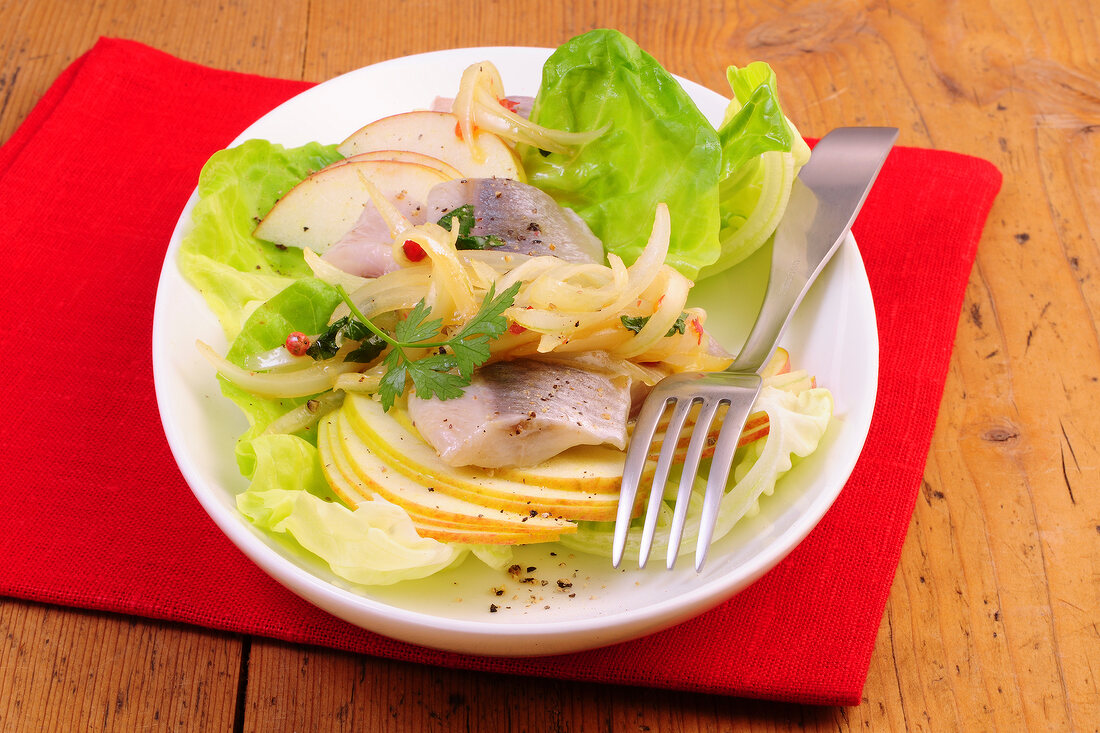 Marinated herring with apple and lettuce on plate with fork
