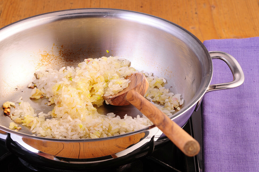 Risotto rice with shallots being roasted in wok, step 1