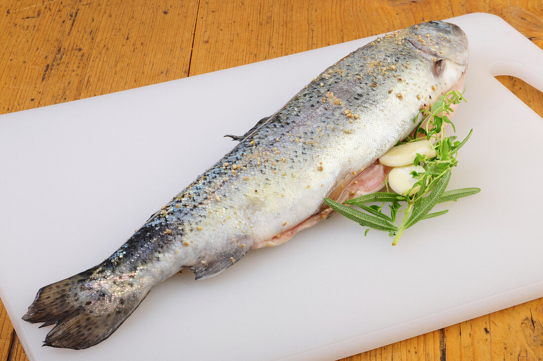 Raw trout fish with filling of herbs on chopping board, step 1