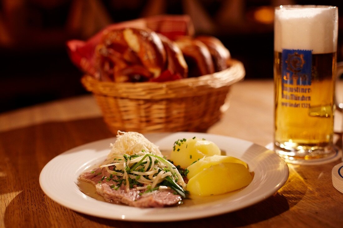 Meat, potatoes and radish on plate and basket of pretzels on wooden table
