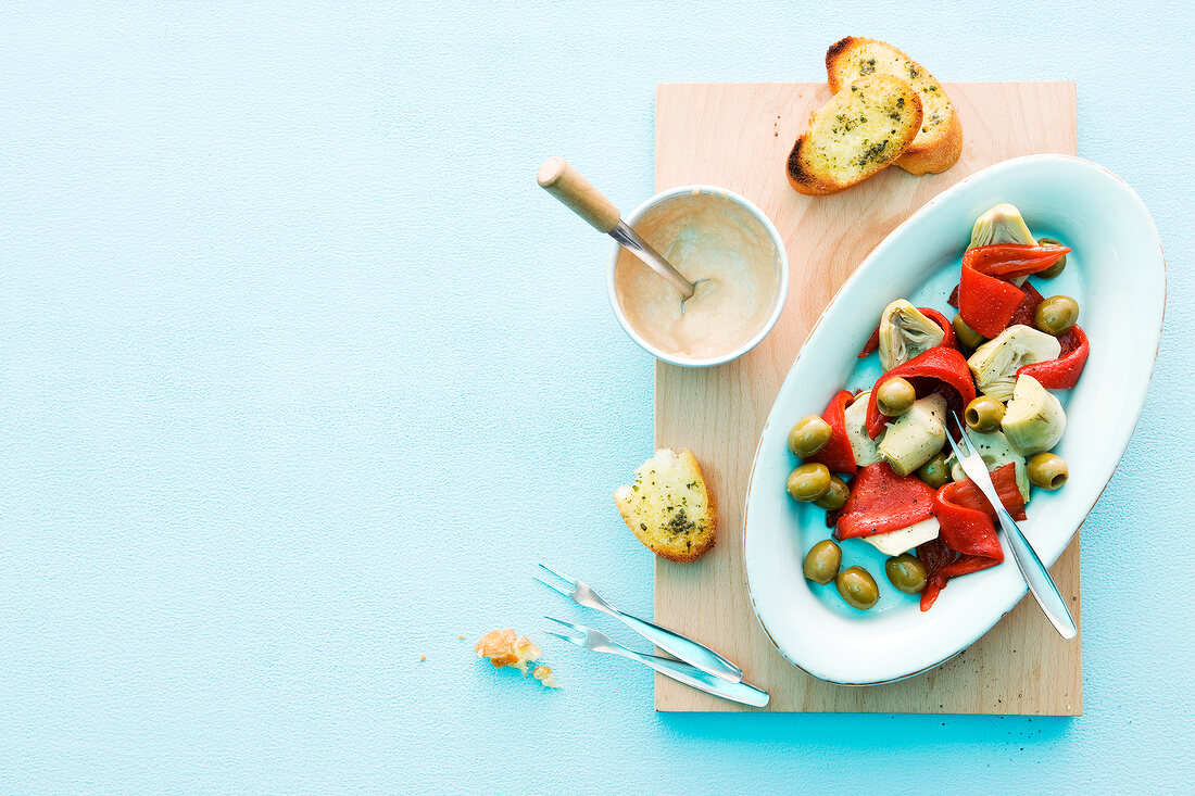 Antipasti with tuna sauce and herb bread on plate and wooden board, overhead view