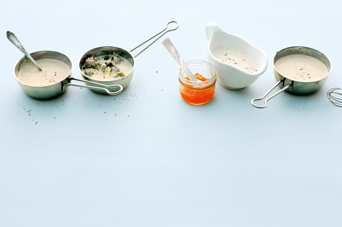 Four different cream sauces for pasta in saucepans and sauceboat