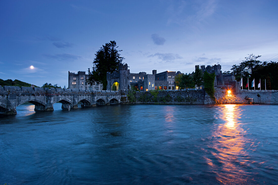 Illuminated Ashford Castle and Bridge over Cong canal at dusk, Ireland, UK