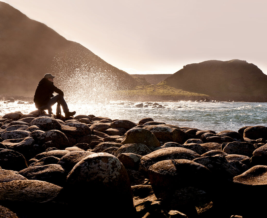 Man sitting on rocks and looking at sea in Giant's Causeway, Ireland