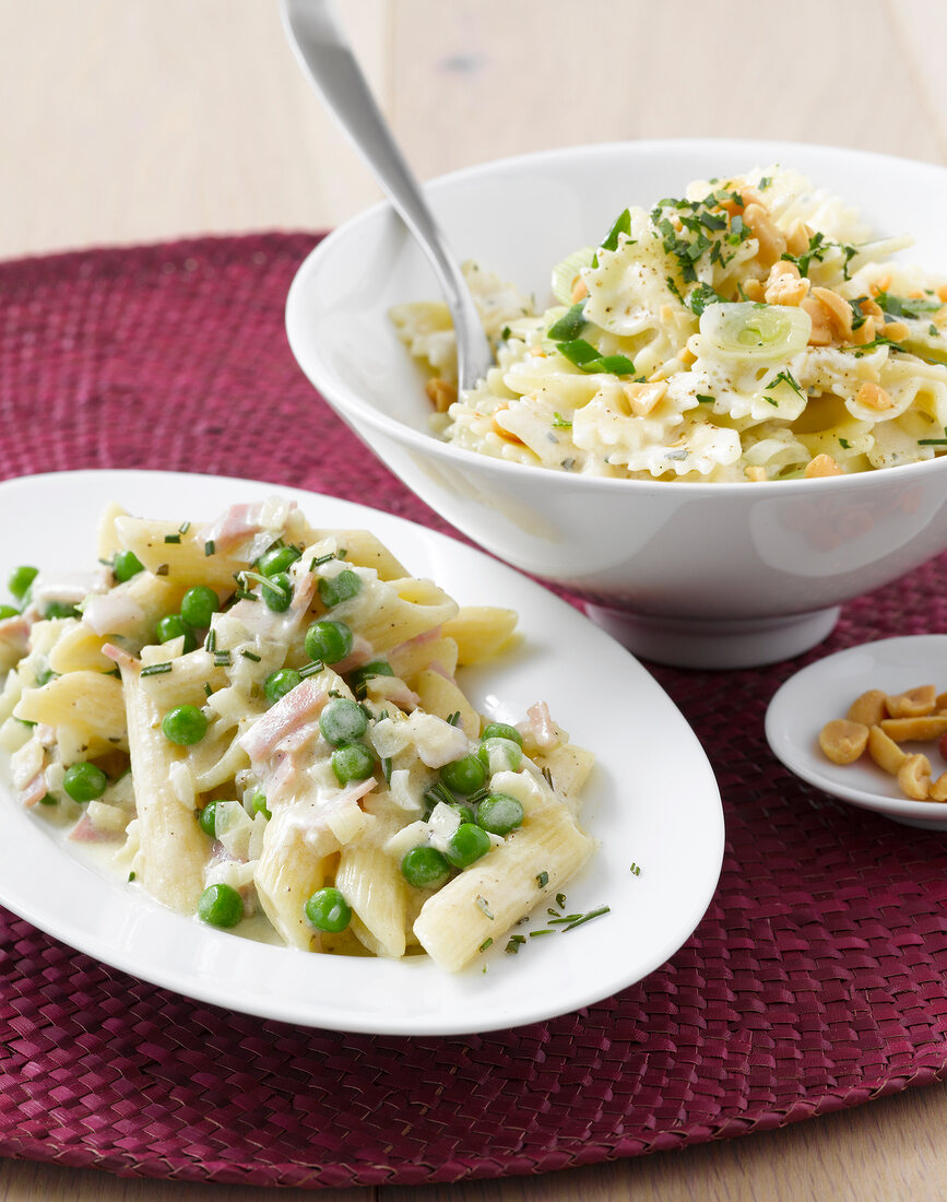 Ham pasta with peas on plate and farfalle with cheese sauce in bowl