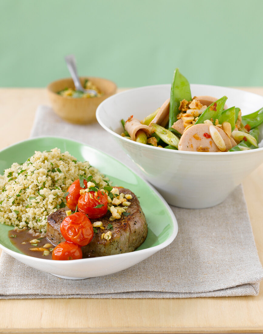 Steak with almond and gremolata in serving dish and sausage salad in bowl