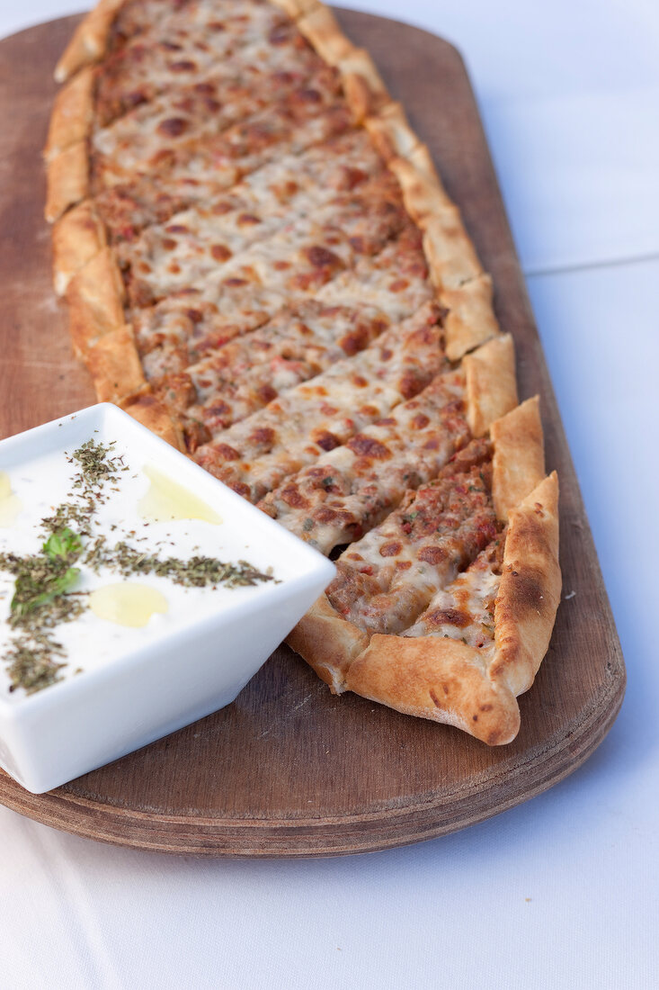 Slices pizza with yogurt and cucumber sauce in bowl on wooden tray