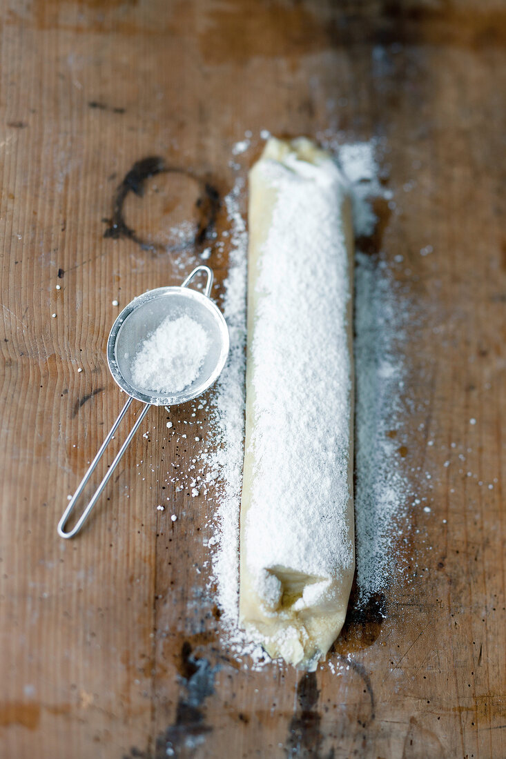 Apple roll filoteig and thick layer of icing sugar on it with strainer on wooden surface