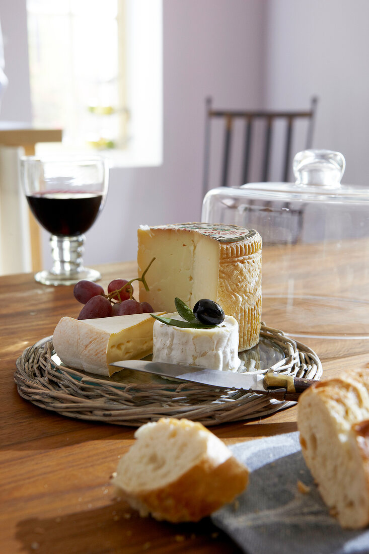 Cheese, baguette, wine, and glass cloche on wooden table