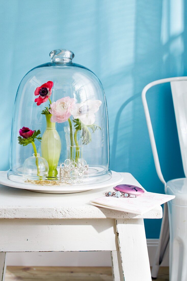 Glass cover over three small vases of anemones and ranunculus