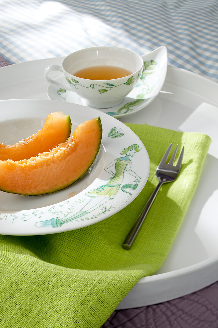Plate of sliced fruit on tablecloth with bowl of sauce on tray