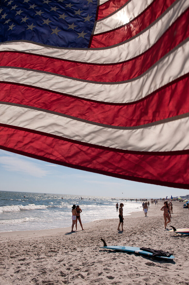 American flag waving with people enjoying on beach, New York, USA