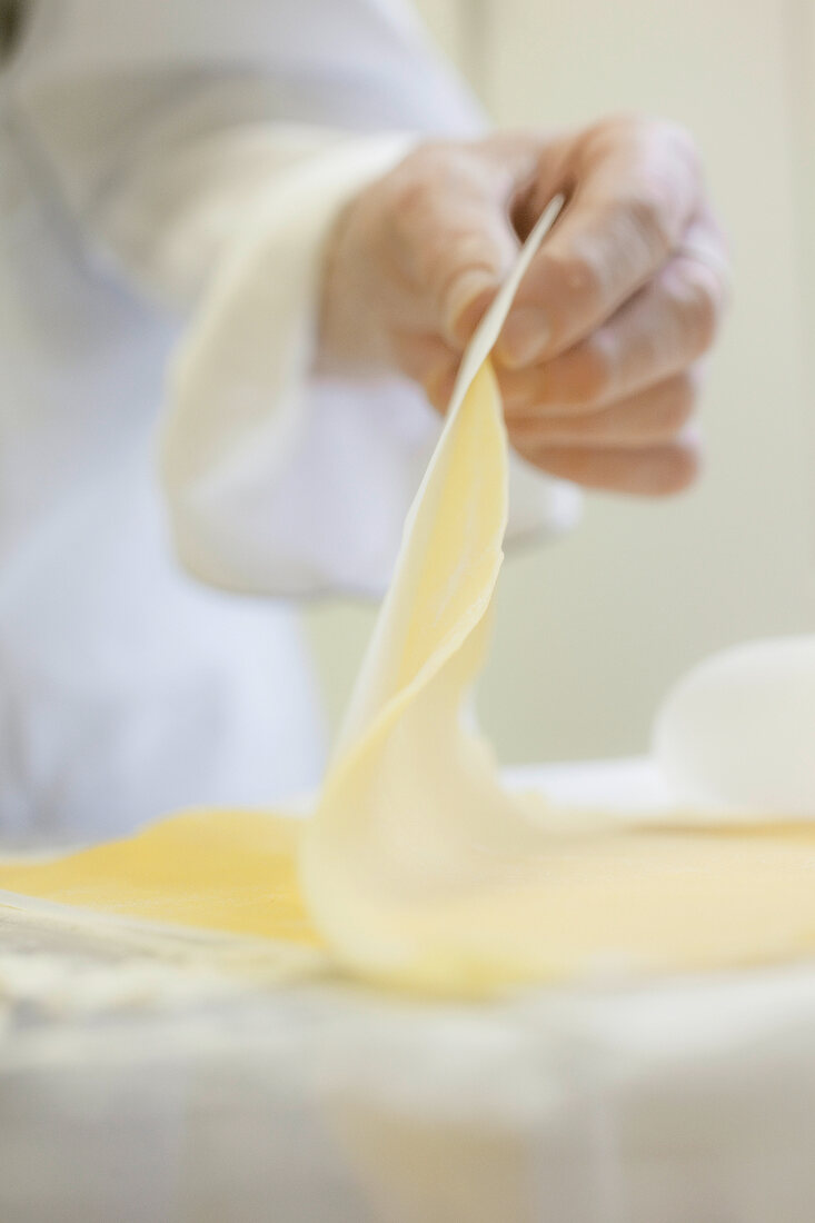 Close-up of hands holding rolled out pasta dough