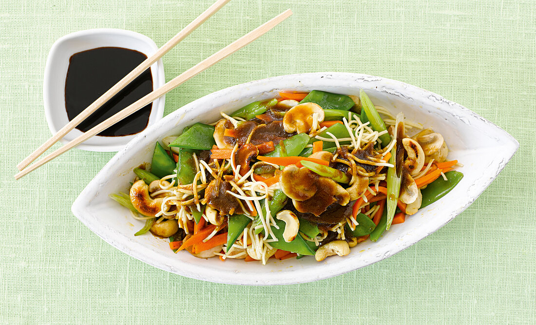 Noodles with vegetable in serving bowl and curry in small bowl with chopsticks on it