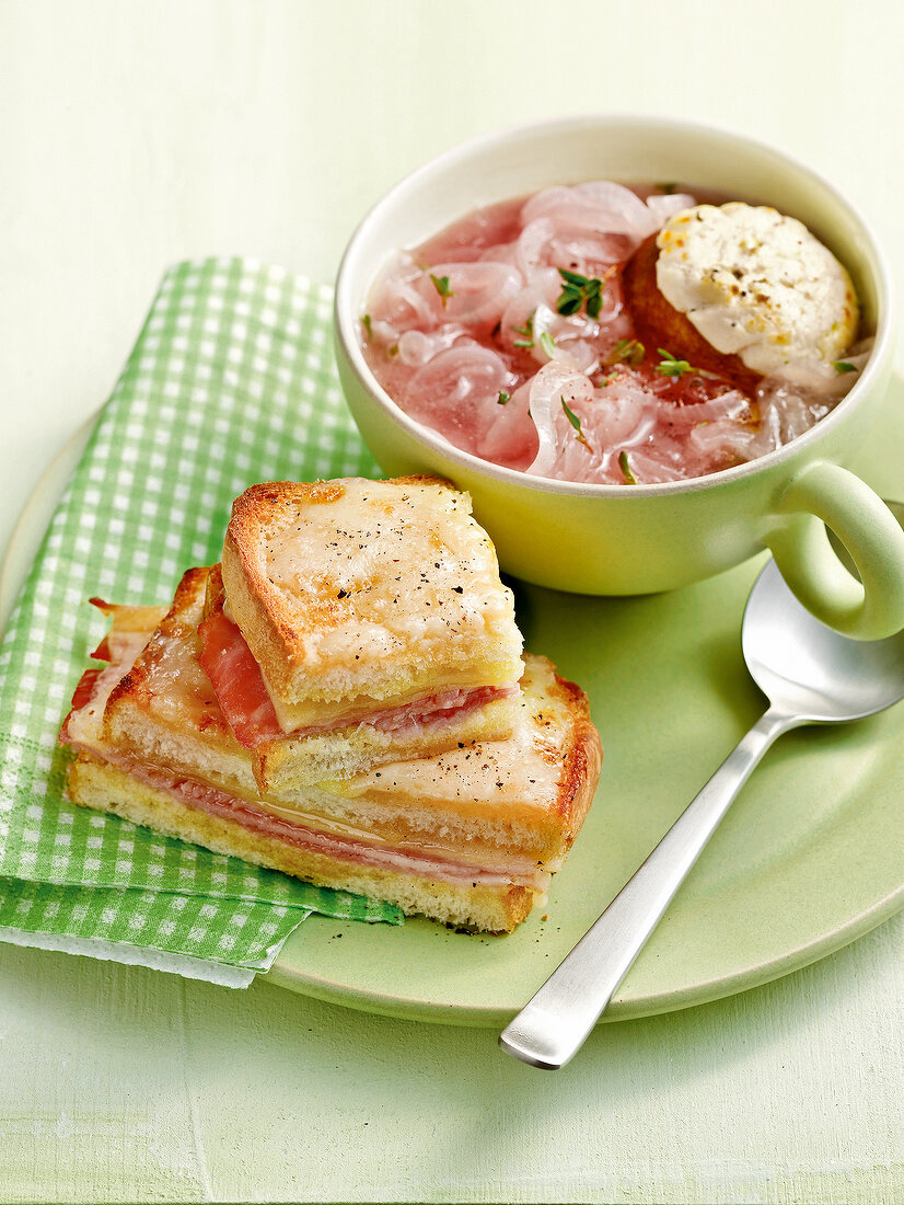 Red onion soup with croutons in cup and croque monsieur on plate
