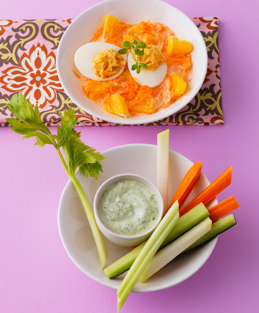 Stuffed eggs in carrot salad, raw vegetables with quark dip on pink surface