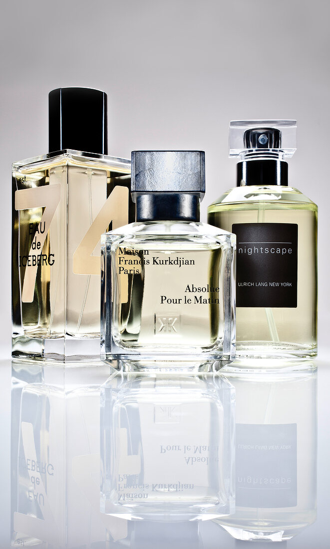 Close-up of three perfume bottles and reflection on white background