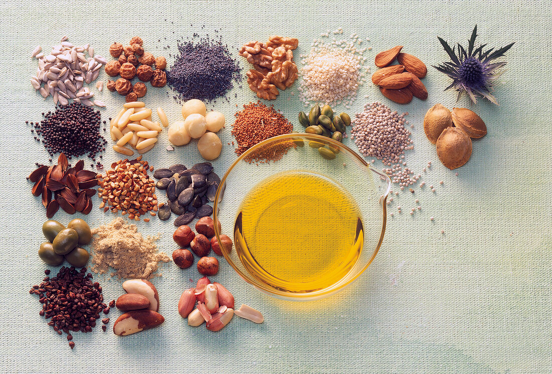 Various nuts and bowl of oil on gray background