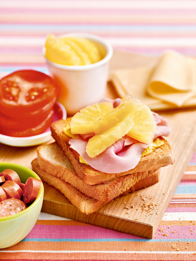 Slices of toast topped with ham and pineapple on wooden cutting board