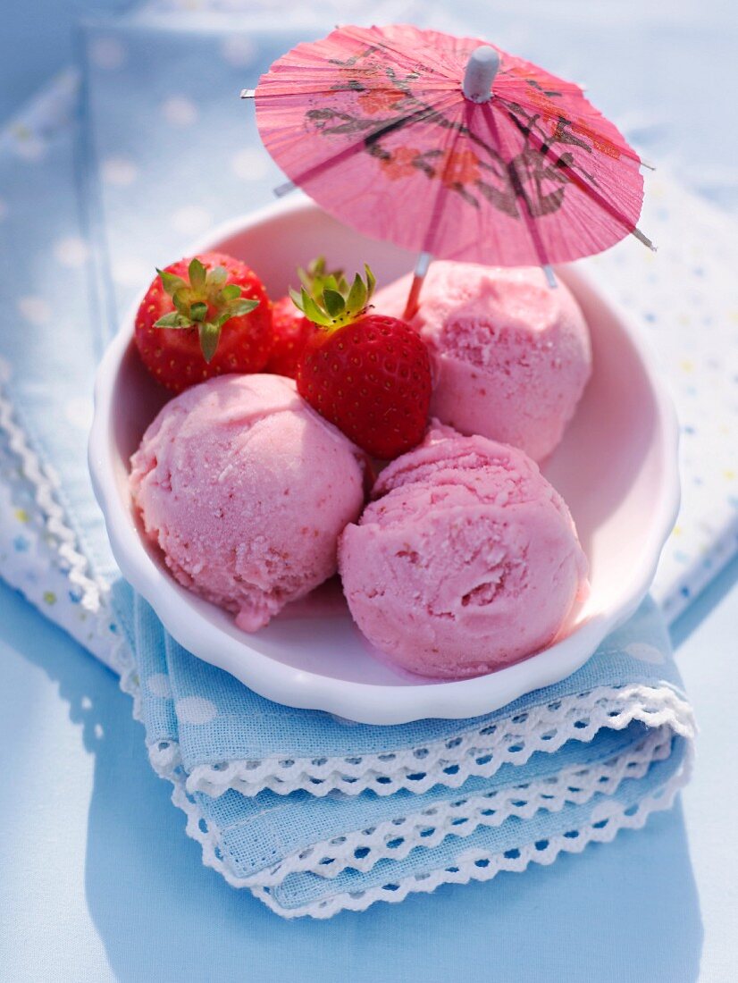 Three scoops of strawberry ice cream with fresh strawberries and a cocktail umbrella