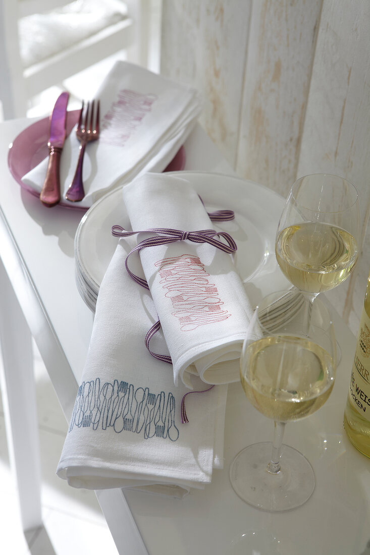 Rolled white cloth napkin with stamped designs and wine glasses on side