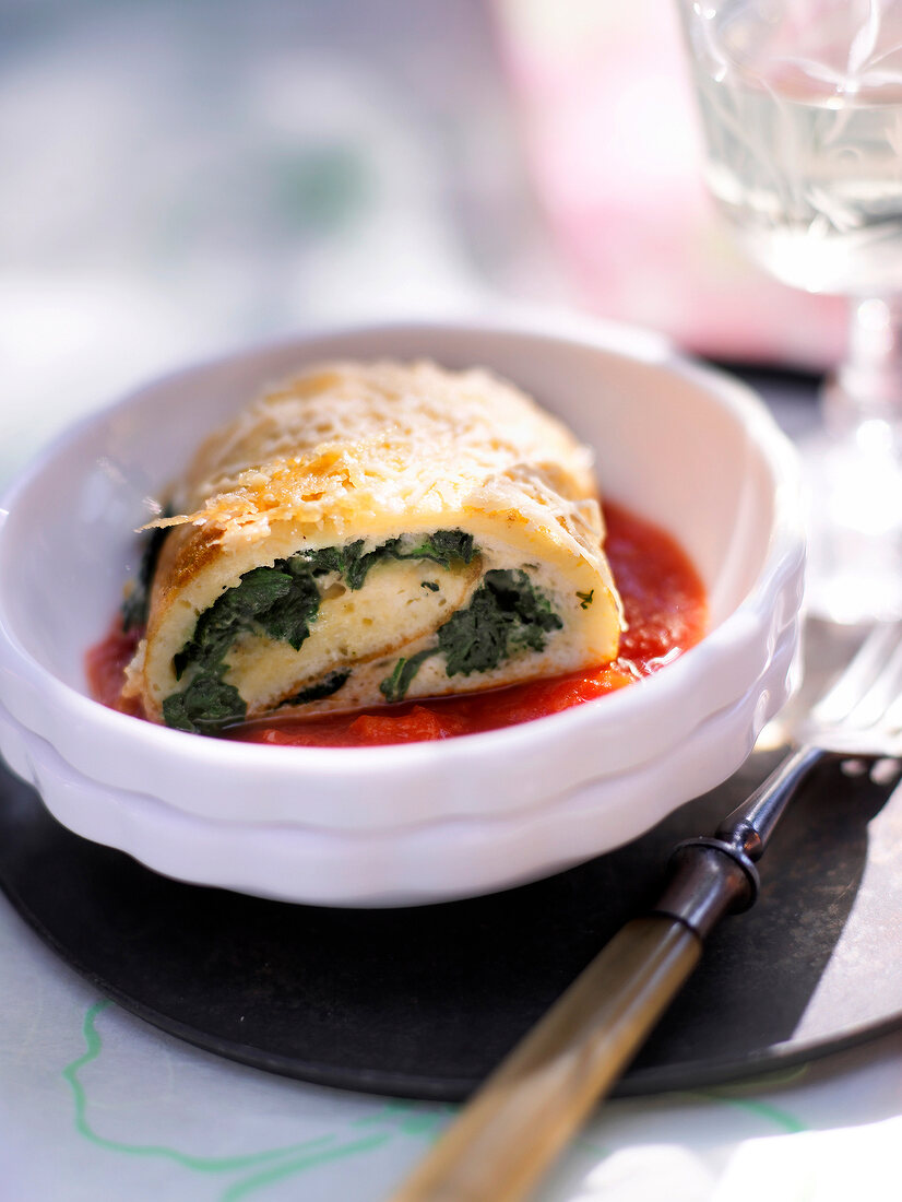 Omelette roll with spinach and tomato sauce in serving dish