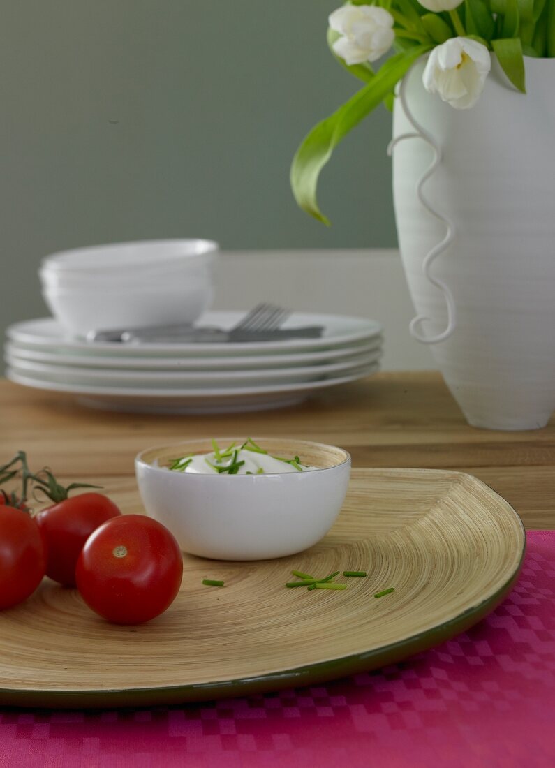 Tomatoes on wooden plate and cream in plate on pink table mat