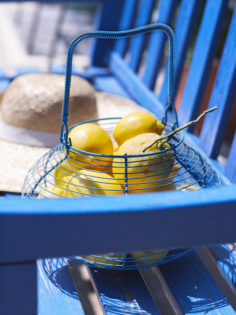 Blue basket with lemon and straw hat on wooden bench