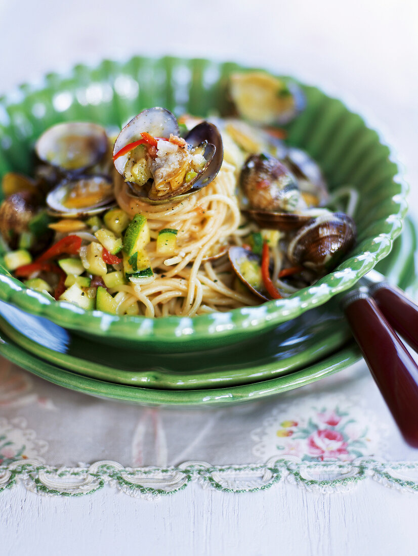 Spaghetti served with clams and courgettes in green bowl in summer kitchen