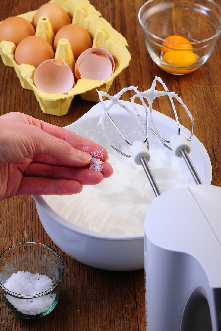 Salt being added to beaten egg whites in bowl while preparing dessert