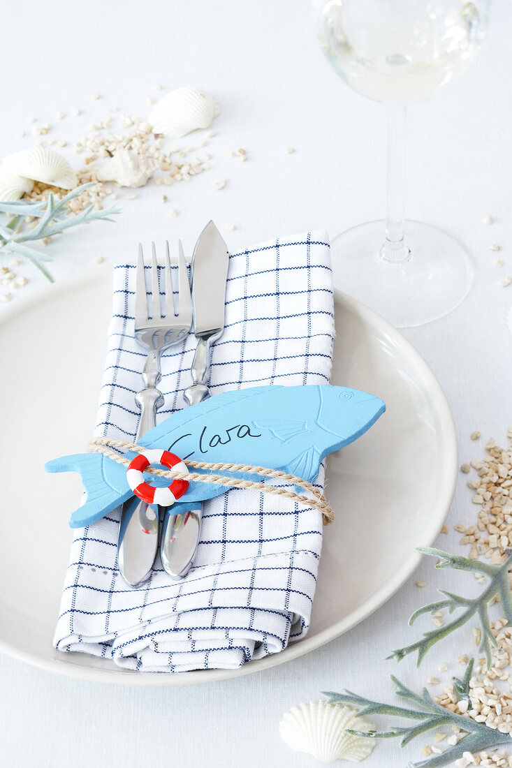 Close-up of plate, napkin, cutlery and wooden blue fish with name tag