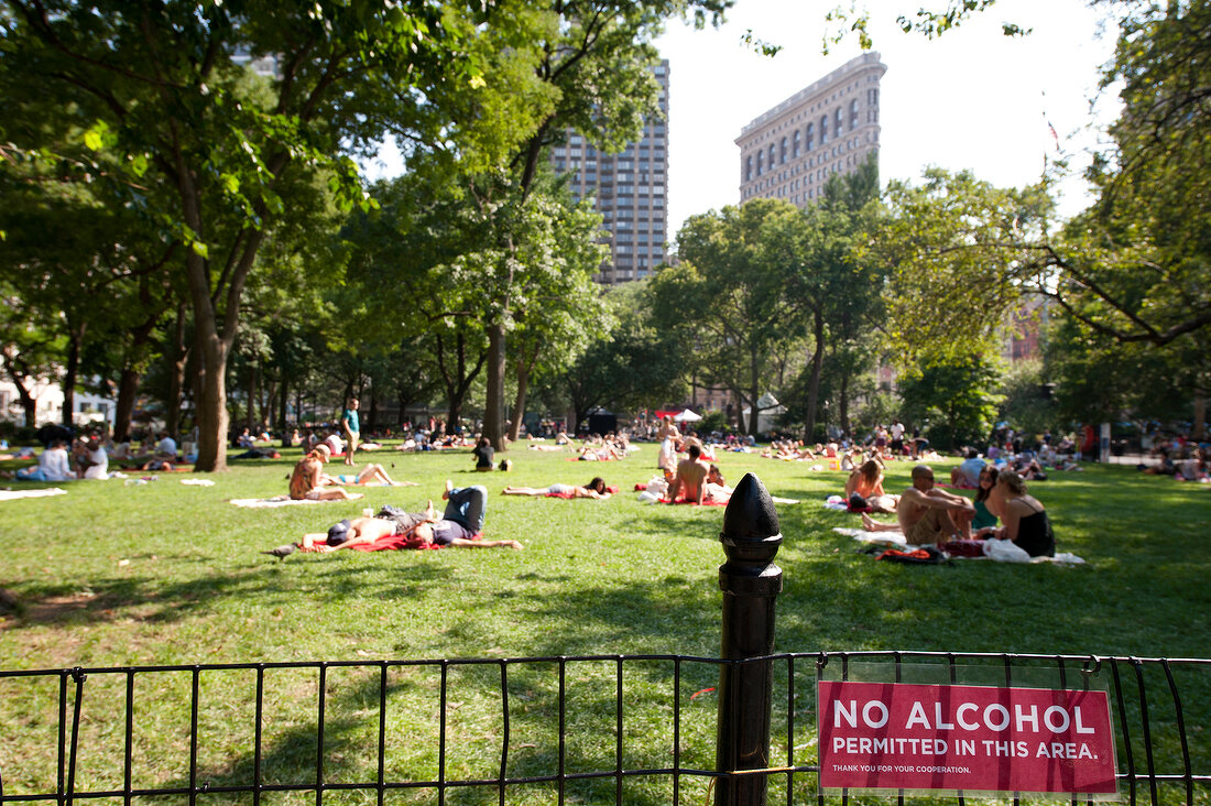 People relaxing in Madison Square Park overlooking skyscrapers, New York, USA