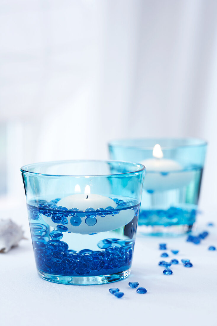 blaues Teelichtglas gefüllt mit Wasser und blauen Glassteinchen