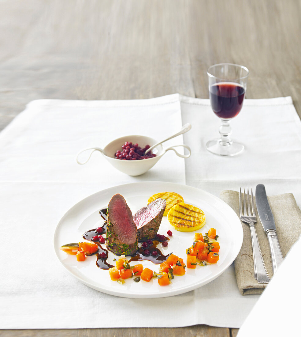 Venison served with pumpkin confit, semolina slices and cranberries on plate