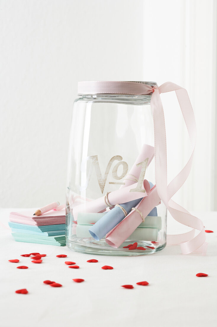 Papierröllchen mit kurzen Briefen in einem Glas, rosa Bändchen