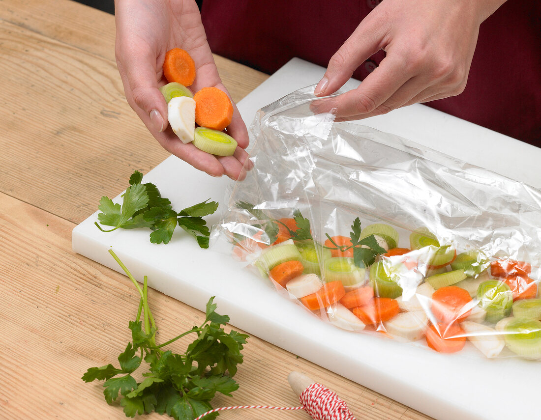 Close-up of hands filling vegetables in plastic bag on cutting board