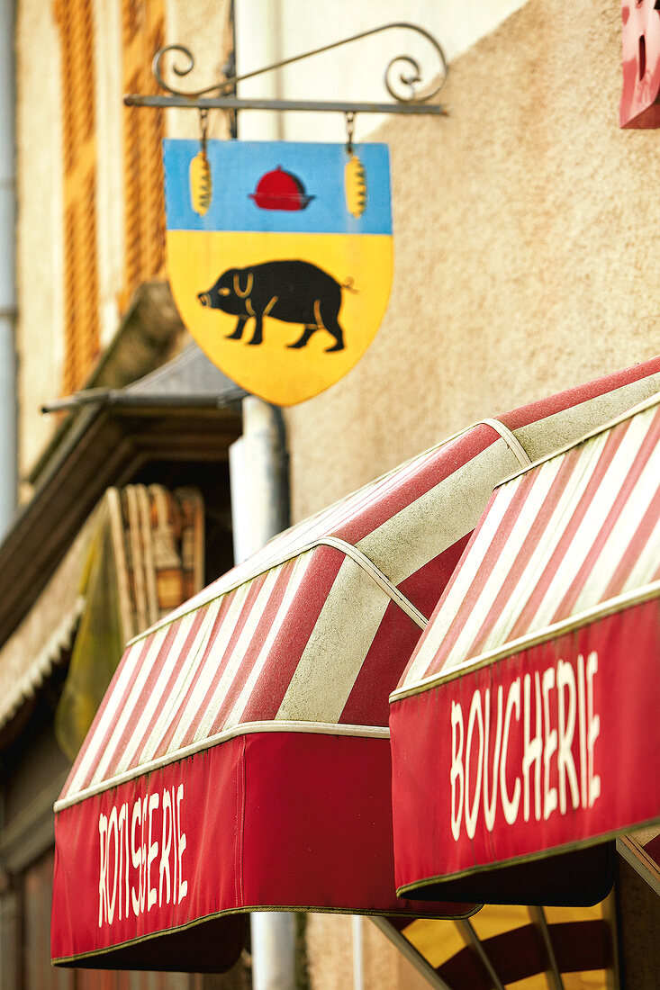 Shield shaped signboard with pig sign hanging outside French butcher shop, France