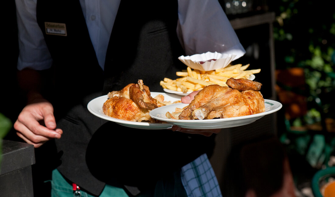 Kellner trägt halbe Hähnchen und Pommes frites, Schweizerhaus