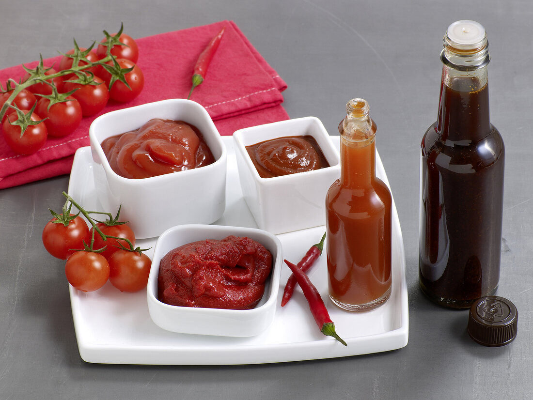 Various types of sauces in bowls and bottles with cherry tomatoes