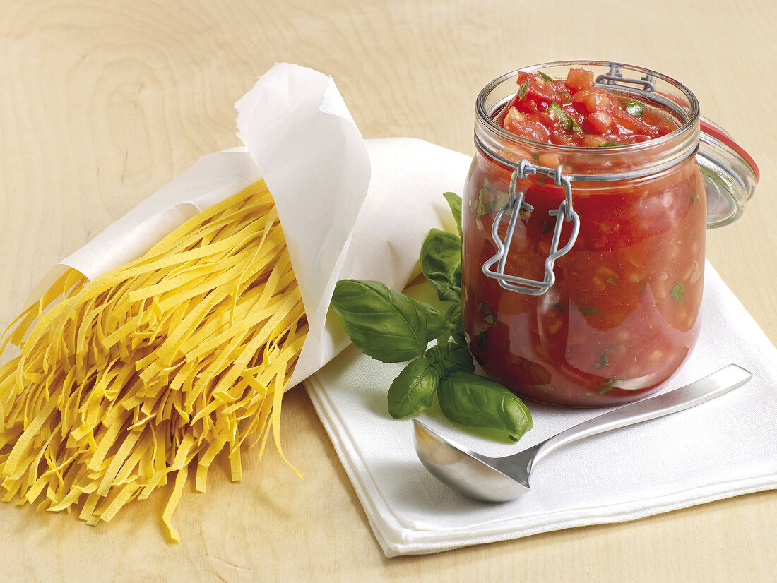 Glass jar with tomato sauce and raw noodles