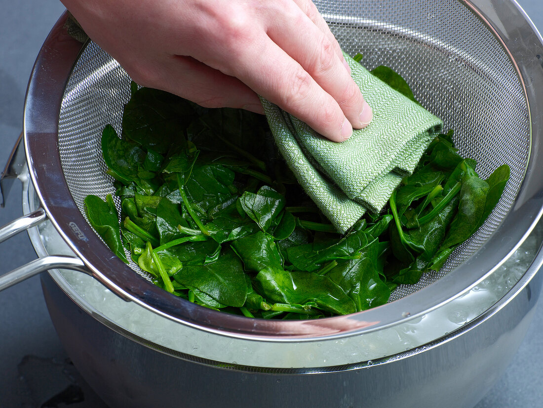 Close-up of hand wiping blanched spinach with napkin for preparation of sauce, step 3